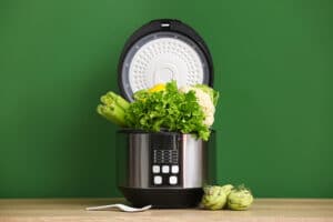 modern multi cooker with vegetables on table against color background