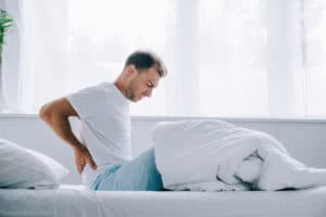 man suffering from back pain while sitting on bed
