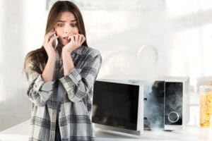 scared woman talking on a phone near a broken microwave